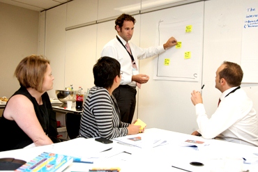 Teachers sit at a whiteboard and work collaboratively
