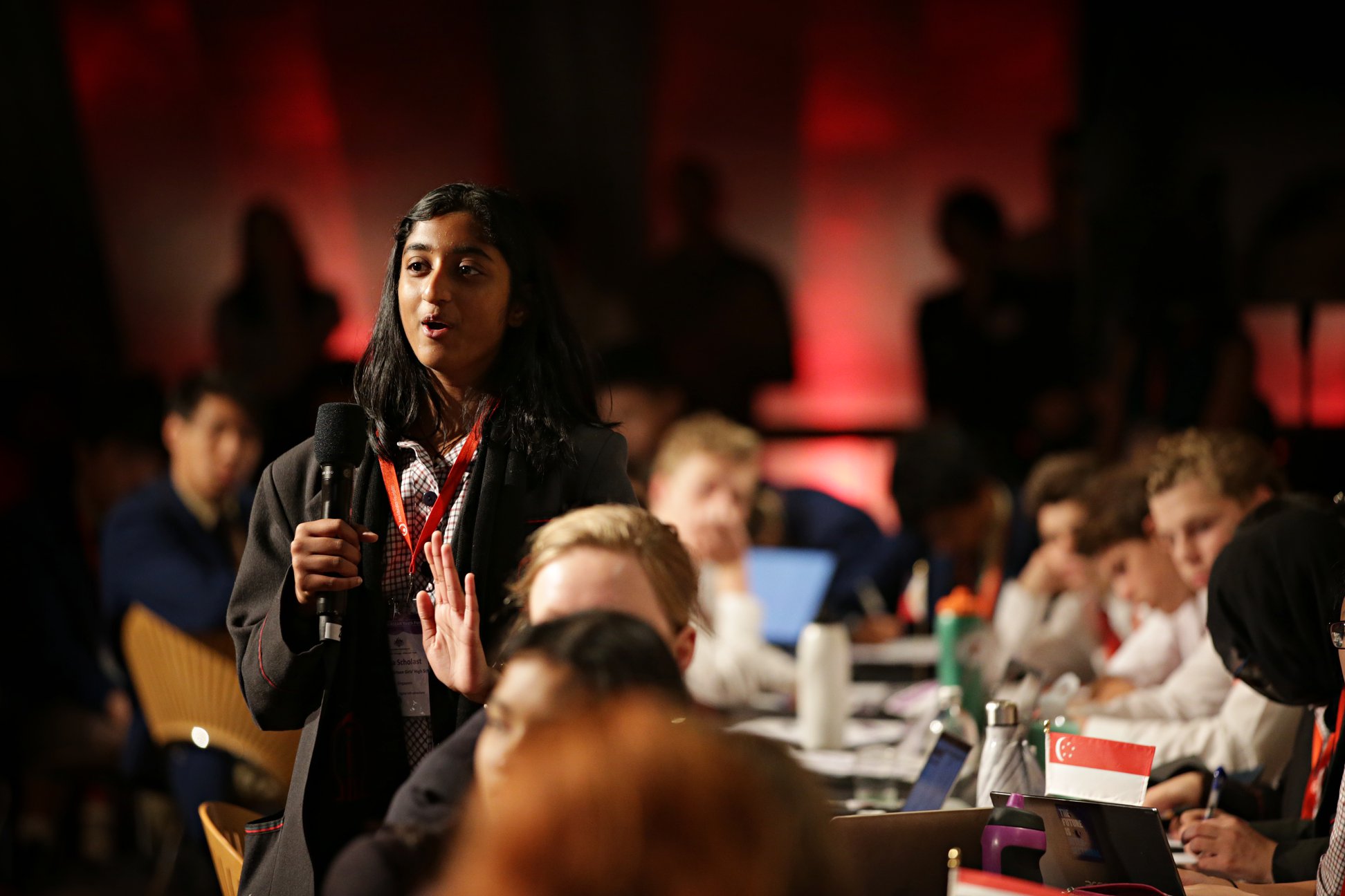Students stands with a microphone to address a cohort of their peers 
