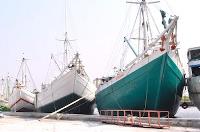 Three old, wooden ships all docked at a harbour by the sea
