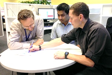 Three men sit and work together at a desk